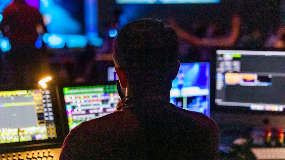 A man standing in front of multiple illuminated computer screens.