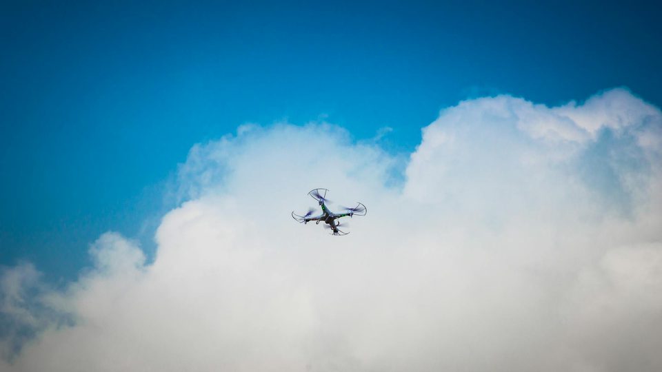A quadcopter drone flying against an overcast sky.