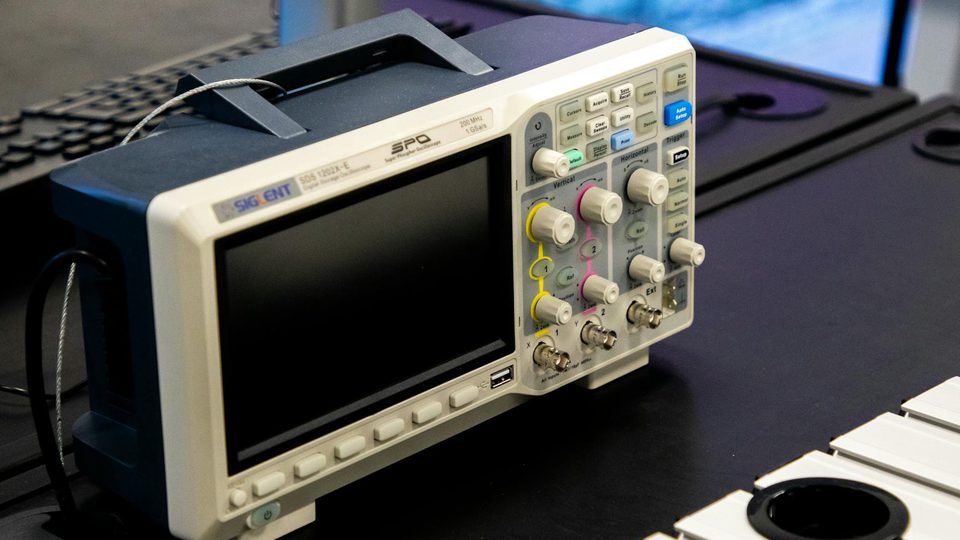 A digital oscilloscope and electronic test equipment on a workbench.