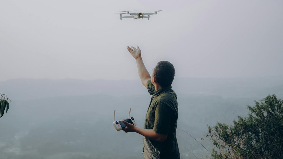 A man controlling a drone outdoors, used as a lead visual for an article comparing cooperative Remote ID and wider RF detection.
