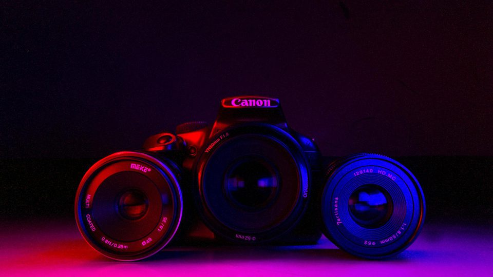 A DSLR camera with multiple lenses arranged on a dark surface.